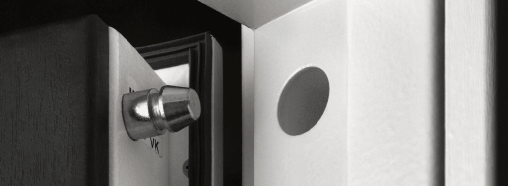 Close-up of a door latch bolt extended toward a strike plate in the door frame, showing the locking mechanism in detail in black and white.