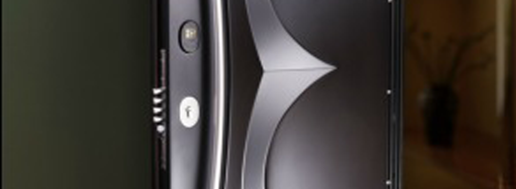 A close-up of a sleek, modern smartphone with a curved back design, featuring a camera, LED flash, and minimalist buttons. The device appears to be standing upright indoors, with a blurred background.