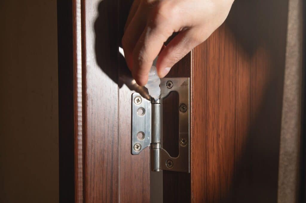 an individual lubricating their door hinges