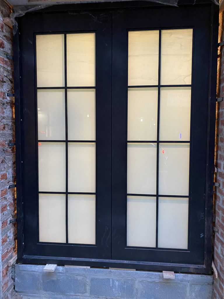Black French doors with frosted glass panes are set into a brick wall.