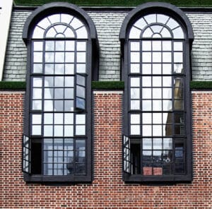 Black arched security windows with grilles installed on a brick building, designed by Shield Security Doors.
