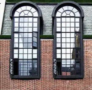 Black arched security windows with grilles installed on a brick building, designed by Shield Security Doors.
