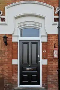 Decorative white front door with glass panel and intricate trim, set in a red brick exterior with vintage lighting and tiled entry steps