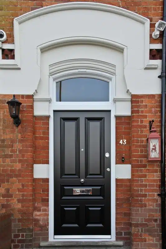 Decorative white front door with glass panel and intricate trim, set in a red brick exterior with vintage lighting and tiled entry steps