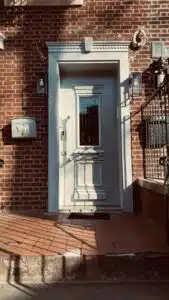 Decorative white front door with glass panel and intricate trim, set in a red brick exterior with vintage lighting and tiled entry steps