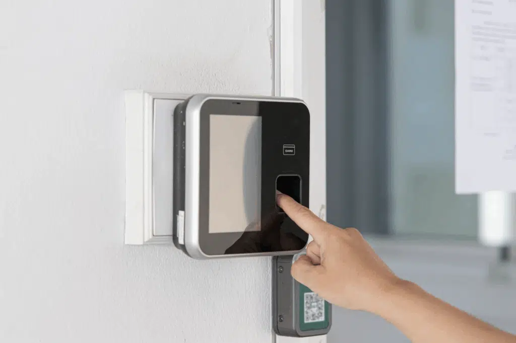 A hand presses a finger against a biometric fingerprint scanner on a gray wall