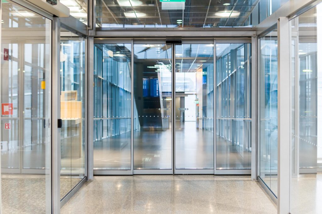 Modern glass entrance with sliding doors, leading to a bright hallway.