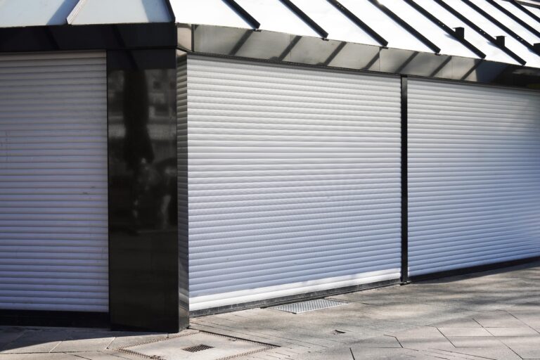 Closed white roller shutters cover the front of a storefront
