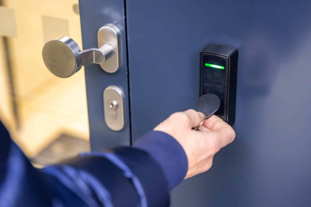 A person in a navy jacket unlocks a modern, metallic door using a key fob near an electronic access control pad