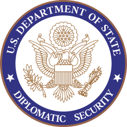 Seal of the U.S. Department of State Diplomatic Security, featuring a bald eagle holding an olive branch and arrows, with a shield and a banner surrounded by blue and gold circular text.