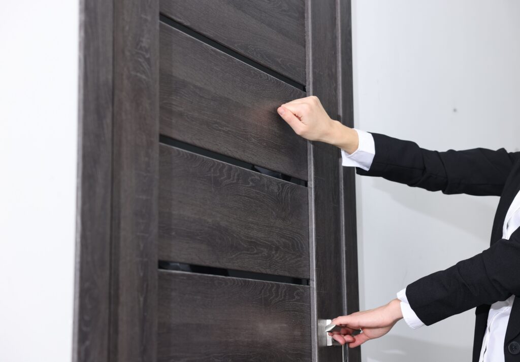 an individual knocking and trying to open a high security modern front door to a home.
